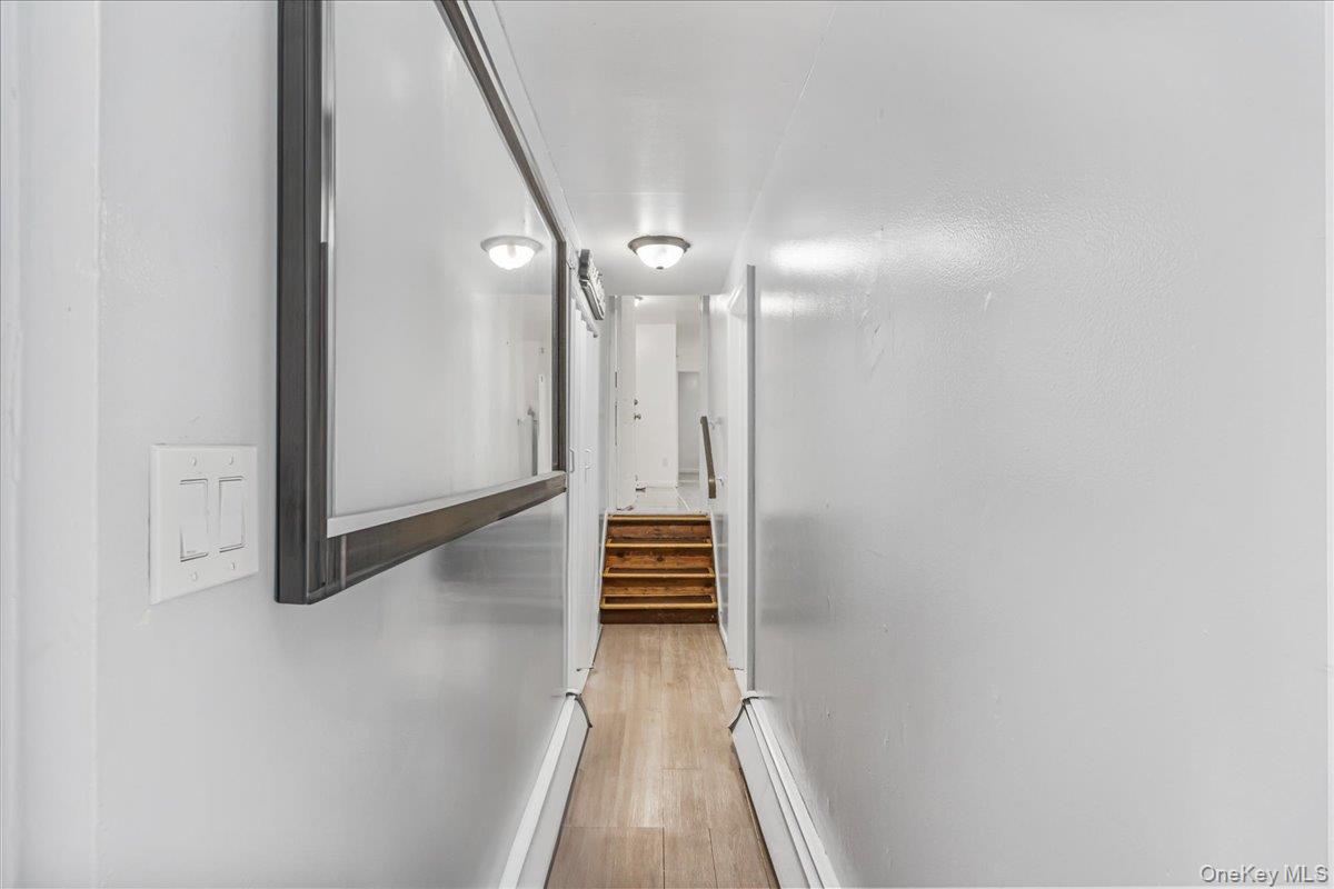 132-14 Horace Harding Expressway Queens, NY 11367 - Photo 3 of 25 Corridor featuring baseboard heating, stairway, light wood-style flooring, and a baseboard radiator