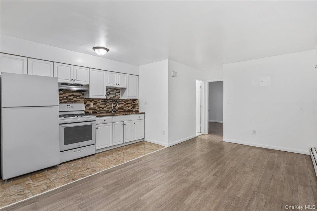 132-14 Horace Harding Expressway Queens, NY 11367 - Photo 5 of 25 Kitchen with white appliances, white cabinetry, decorative backsplash, light wood finished floors, and dark countertops