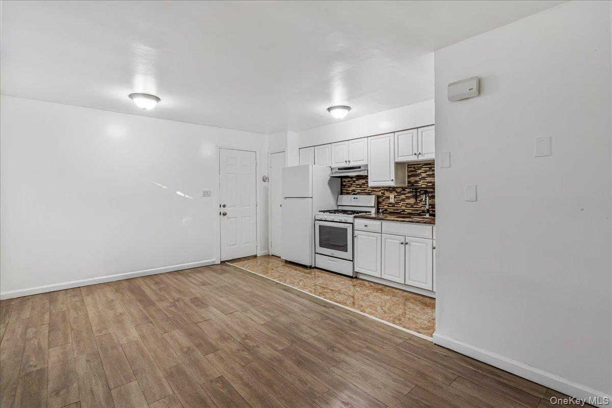 132-14 Horace Harding Expressway Queens, NY 11367 - Photo 6 of 25 Kitchen with white cabinets, white appliances, decorative backsplash, light wood-style floors, and dark countertops