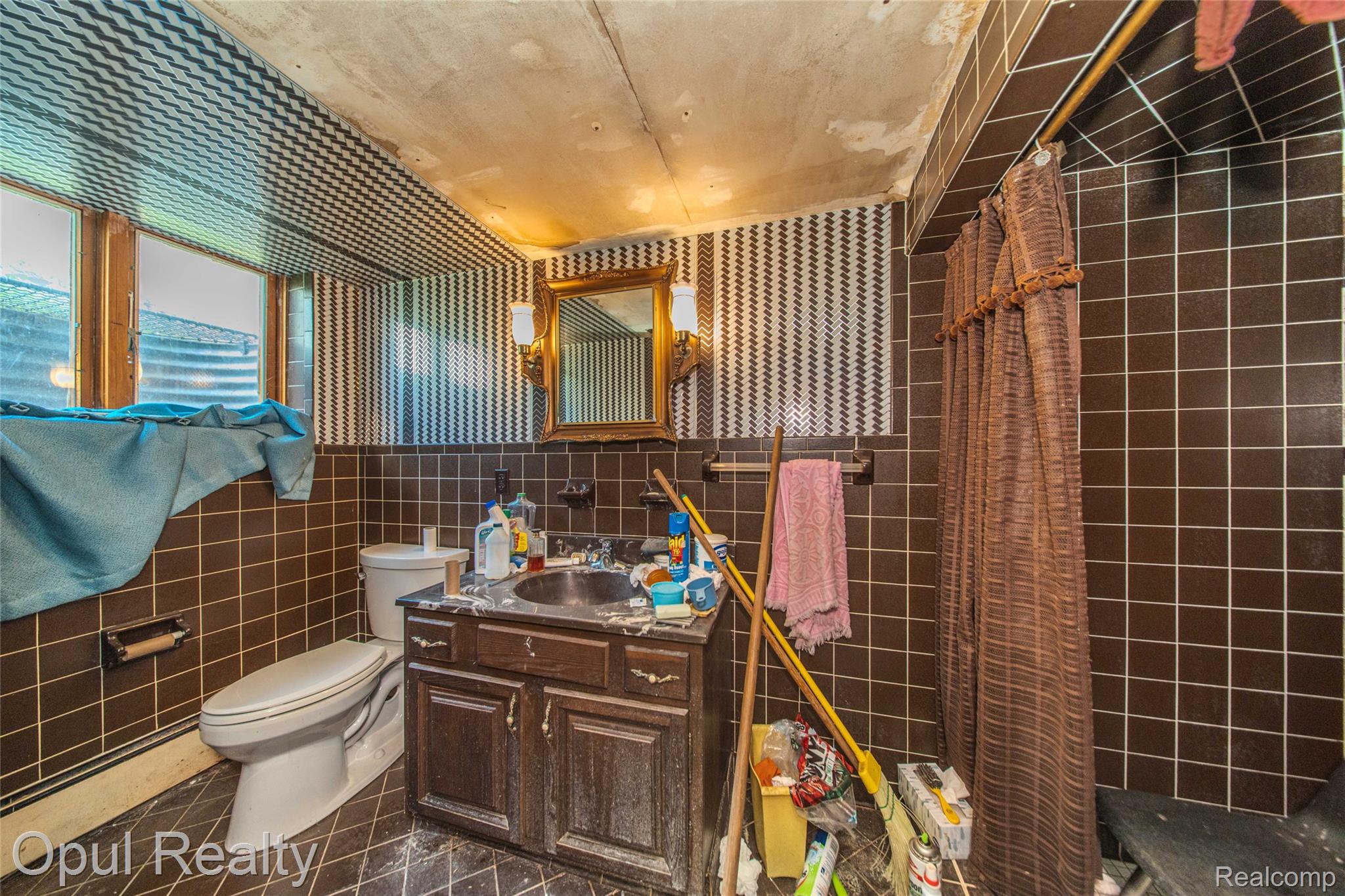 6455 Norham Road Bloomfield Hills, MI 48301 - Photo 61 of 93 Bathroom featuring brown square floor and wall tiling, a built-in shower area, a vanity with a dark wood-finish cabinet and integrated sink, and an ornate gold-framed mirror with sconce lighting
