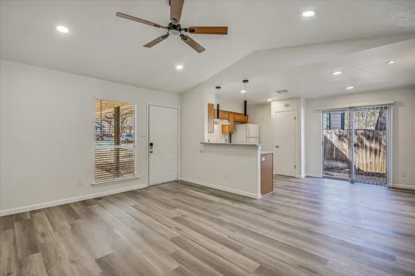 a view of an empty room with wooden floor and a ceiling fan