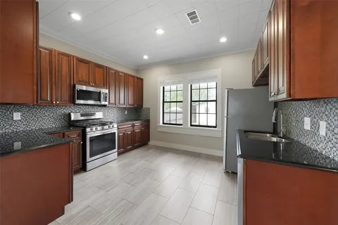 a kitchen with granite countertop a stove top oven a sink dishwasher and a refrigerator with wooden cabinets