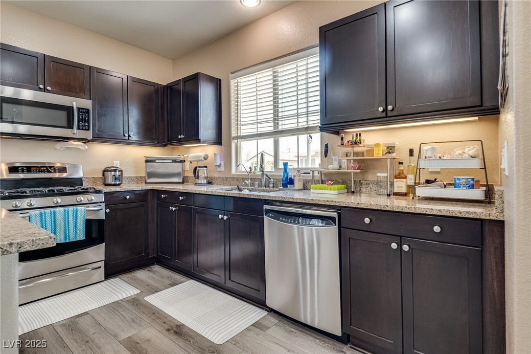 10519 Mann Street Las Vegas, NV 89141 - Photo 18 of 48 Kitchen with appliances with stainless steel finishes, a sink, light wood-style flooring, and light stone countertops