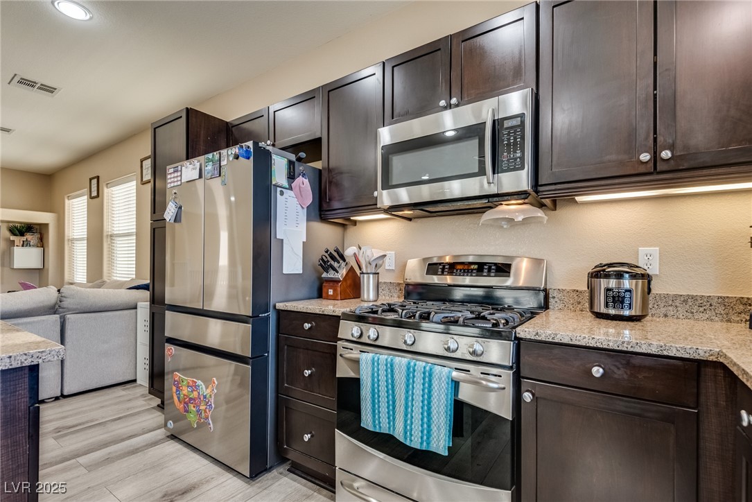 10519 Mann Street Las Vegas, NV 89141 - Photo 43 of 48 Kitchen featuring stainless steel appliances, dark brown cabinets, light wood-style floors, light stone counters, and open floor plan