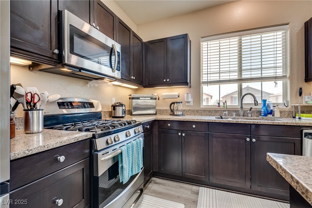 10519 Mann Street Las Vegas, NV 89141 - Photo 19 of 48 Kitchen featuring stainless steel appliances, a sink, dark brown cabinetry, light stone countertops, and light wood-type flooring