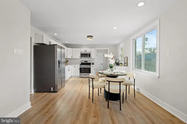 a kitchen with stainless steel appliances a dining table chairs refrigerator and sink