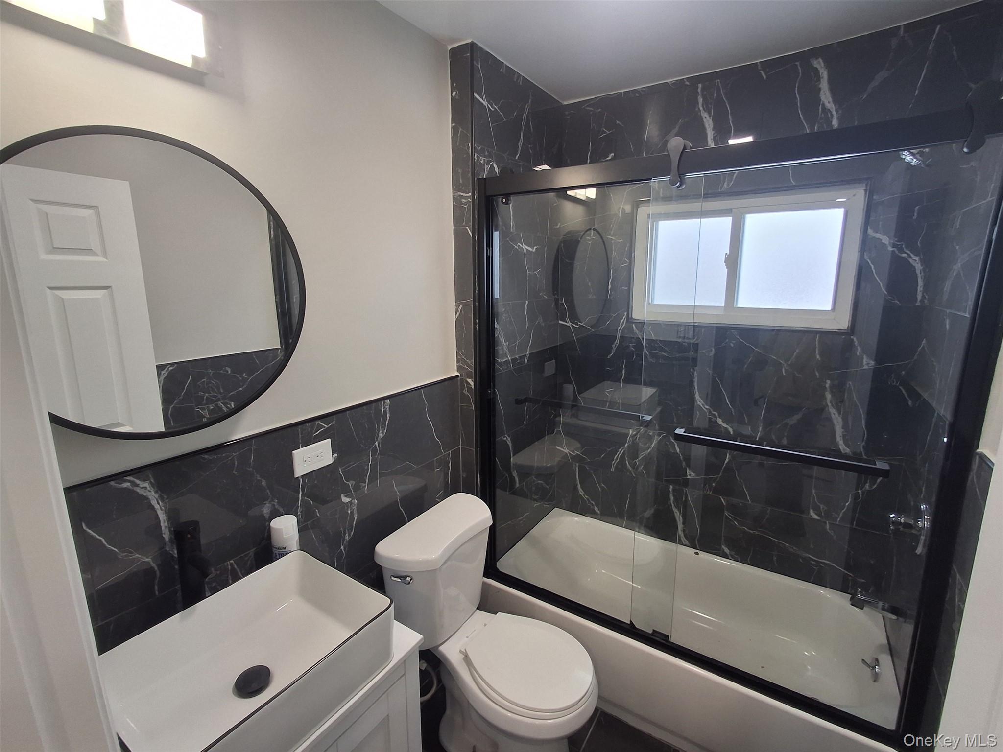 194-14 115th Road, Unit 2 Queens, NY 11412 - Photo 11 of 11 Full bath featuring tile walls, combined bath / shower with glass door, vanity, and wainscoting