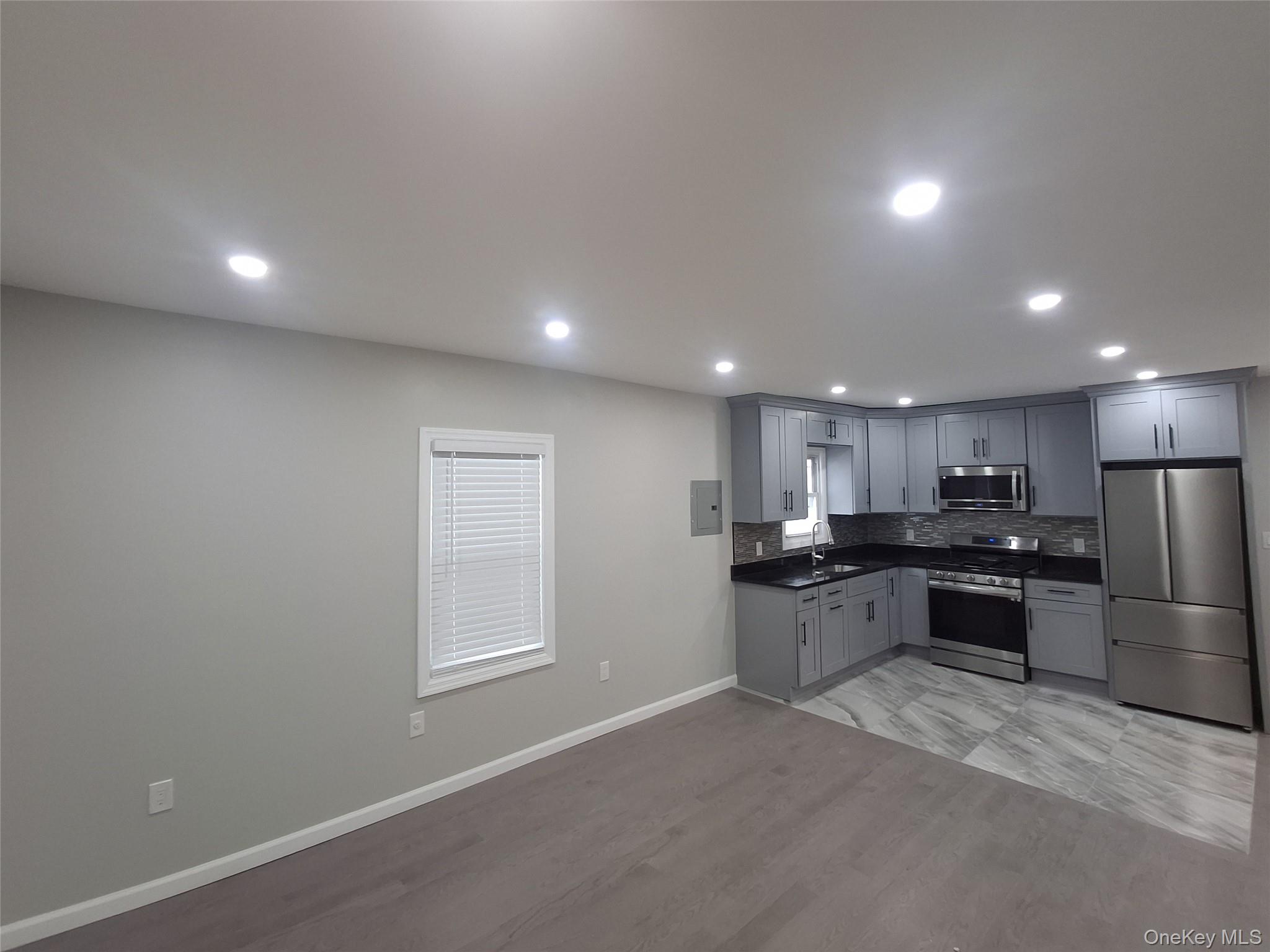 194-14 115th Road, Unit 2 Queens, NY 11412 - Photo 8 of 11 Kitchen with dark countertops, gray cabinets, appliances with stainless steel finishes, light wood-style floors, and decorative backsplash