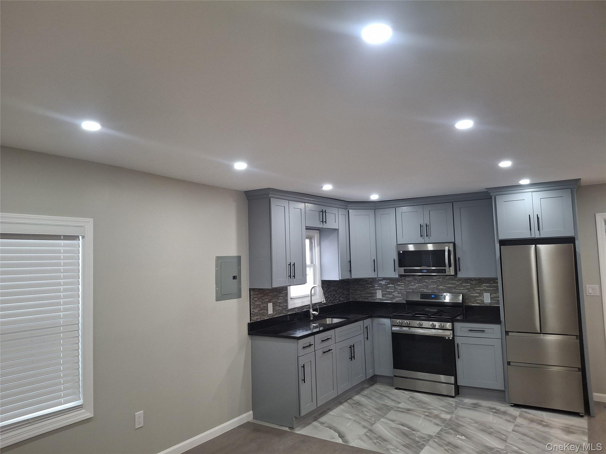 194-14 115th Road, Unit 2 Queens, NY 11412 - Photo 9 of 11 Kitchen with gray cabinetry, appliances with stainless steel finishes, light marble finish flooring, electric panel, and decorative backsplash