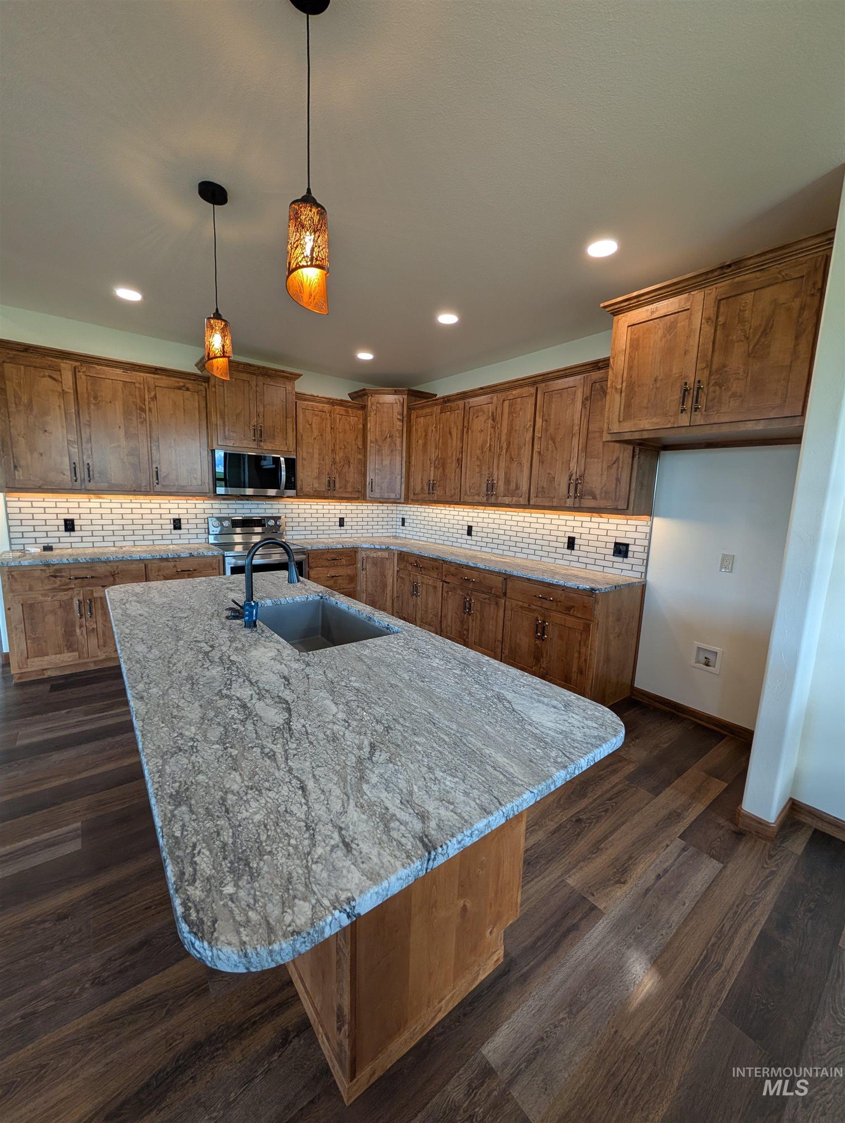 137 Angus Ranch Grangeville, ID 83530 - Photo 7 of 49 Kitchen featuring pendant lighting, brown cabinetry, dark wood-style flooring, backsplash, and appliances with stainless steel finishes