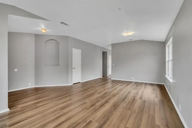a view of an empty room with wooden floor and a window