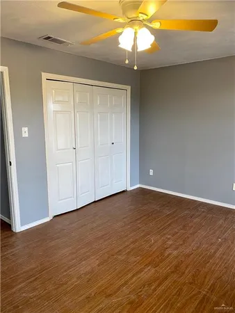 a view of an empty room with wooden floor and a ceiling fan