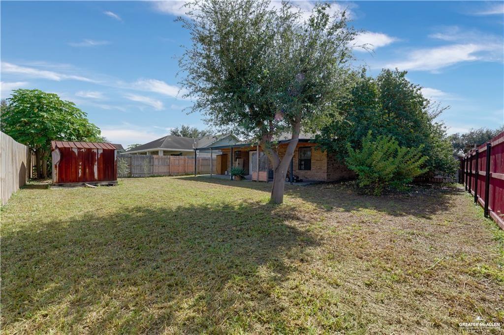 2002 West First Street Mission, TX 78572 - Photo 13 of 14 Spacious backyard with mature shade trees and established landscaping, bordered by red metal fencing on both sides