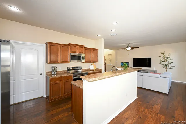 a kitchen with stainless steel appliances a stove top oven a sink a refrigerator white cabinets and wooden floor