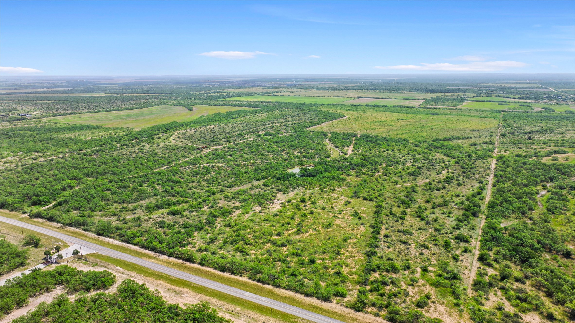0 Fm 2647 Ballinger, TX 76821 - Photo 2 of 17 A vast, verdant landscape with scattered trees, a winding road, and distant fields under an open sky.