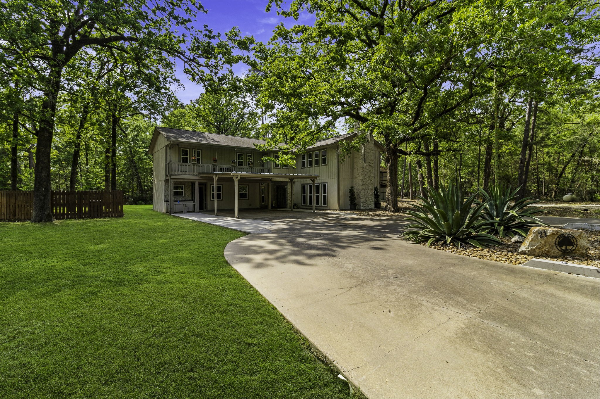 21 Red Oak Circle Point Blank, TX 77364 - Photo 2 of 32 This charming two-story home is set amidst a lush, wooded landscape. The house features a spacious driveway, mature trees, and well-maintained greenery, offering a serene and private setting.