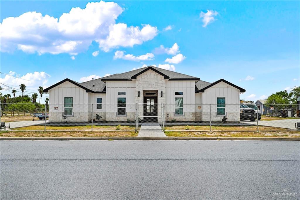 23247 Uresti Road Edinburg, TX 78542 - Photo 17 of 18 White vertical siding, light-colored stone veneer, dark trim, dark roof, and a chain-link fence