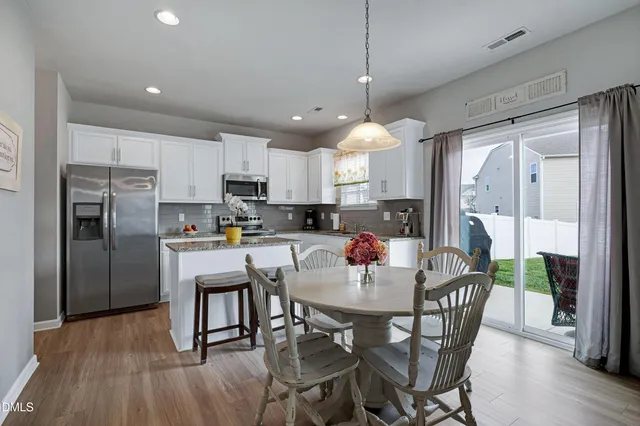 a kitchen with stainless steel appliances granite countertop a dining table chairs refrigerator and microwave