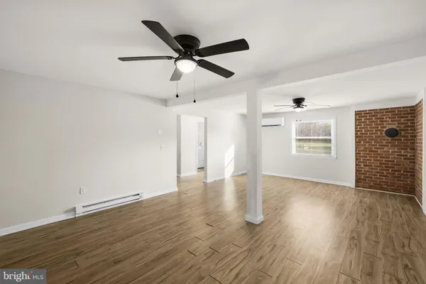 a view of an empty room with wooden floor and a ceiling fan