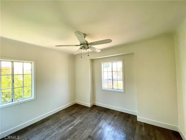 an empty room with wooden floor fan and windows