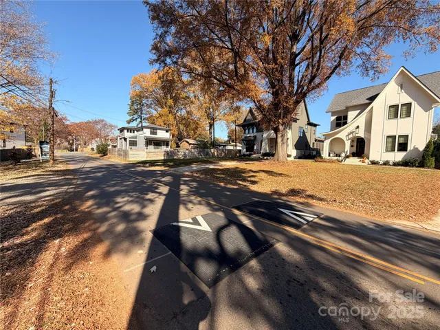 a view of a white house next to a road with large trees