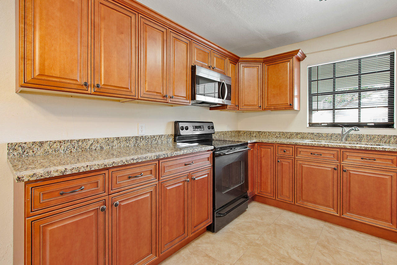 5903 Southeast Mitzi Lane Stuart, FL 34997 - Photo 4 of 22 a kitchen with granite countertop wooden cabinets stainless steel appliances a sink and window