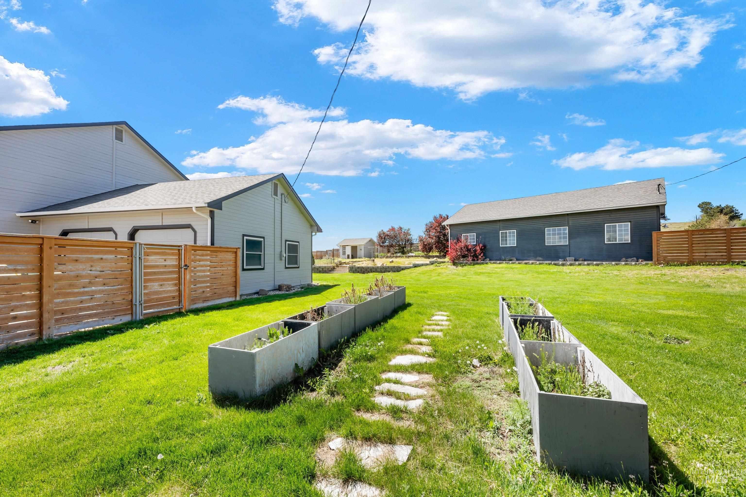 7657 Track Road Nampa, ID 83686 - Photo 31 of 49 Expansive grassy yard featuring a stone pathway, two raised garden beds, and a wood-slat fence