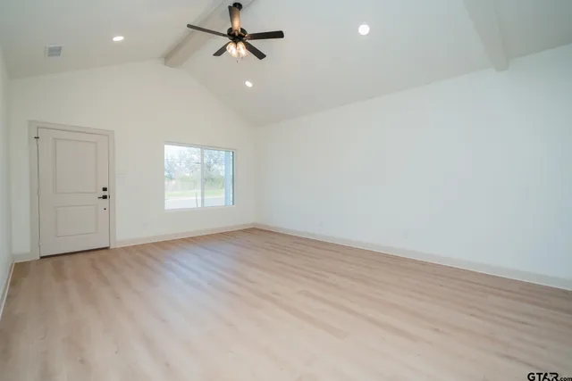 an empty room with wooden floor kitchen view and a window