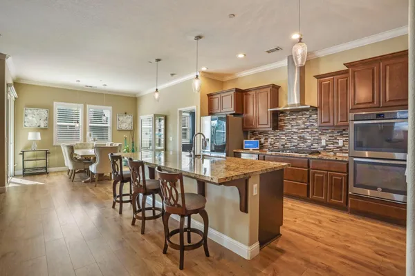 a kitchen with stainless steel appliances granite countertop a stove top oven a refrigerator a sink and white cabinets with wooden floor