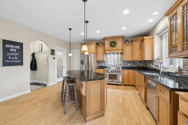 a kitchen with stainless steel appliances kitchen island granite countertop a refrigerator a oven a sink and white cabinets with wooden floor