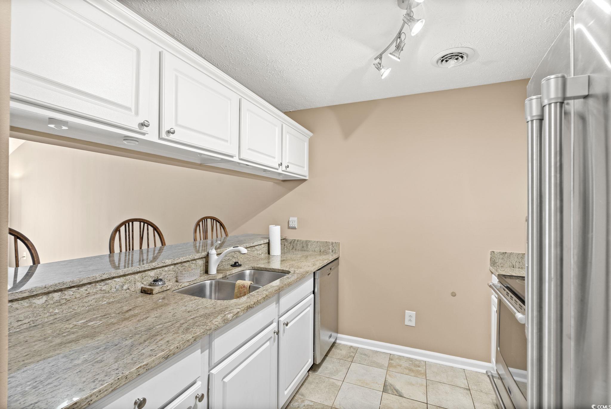 613 14th Avenue South, Unit 34 Surfside Beach, SC 29575 - Photo 12 of 37 Kitchen featuring light stone counters, stainless steel appliances, white cabinets, a textured ceiling, and light tile patterned flooring