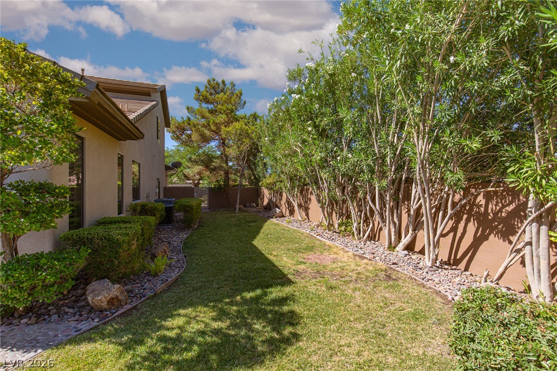 22 Douglas Grove Road Henderson, NV 89052 - Photo 68 of 72 A verdant lawn alongside a privacy wall adorned with thriving greenery, leading to a side yard with mature trees.