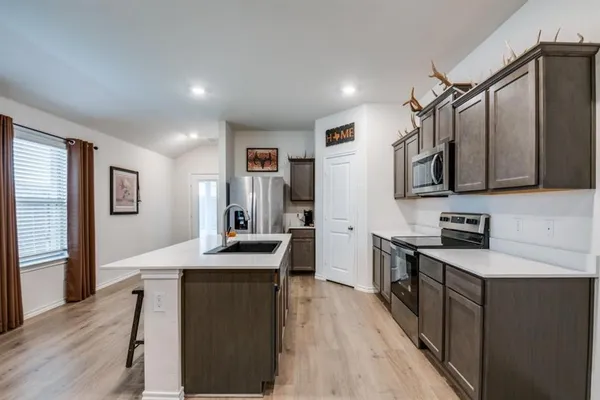 a kitchen with stainless steel appliances a microwave a sink a stove a refrigerator cabinets and a dining table
