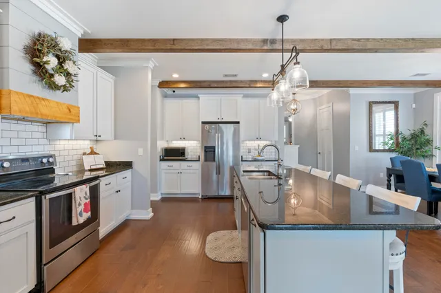 a kitchen with stainless steel appliances kitchen island granite countertop a refrigerator a stove and white cabinets with wooden floor