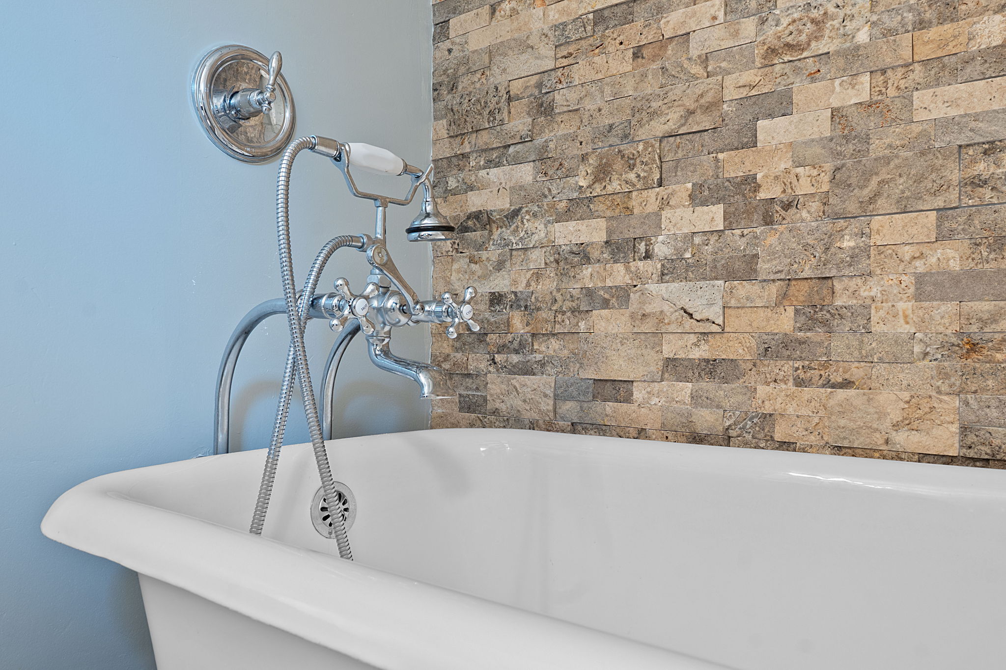 8705 South View Road Austin, TX 78737 - Photo 18 of 39 Close-up of vintage-inspired Clawfoot Tub with polished chrome fixtures and handheld shower against natural Stone tile backdrop.