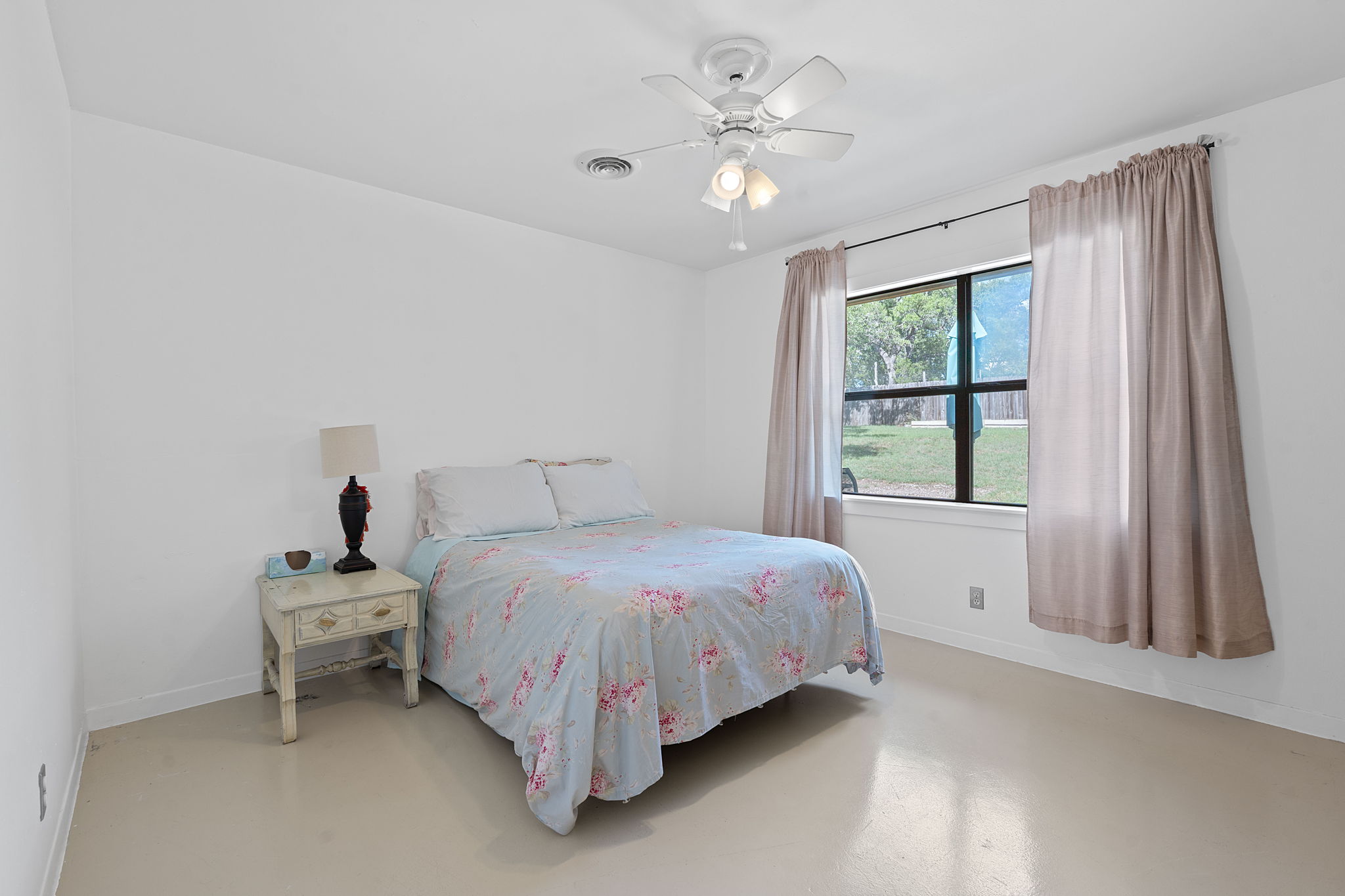 8705 South View Road Austin, TX 78737 - Photo 21 of 39 Cozy Bedroom with neutral walls, Ceiling fan, and Large window overlooking the backyard with Natural Light. Concrete Flooring.