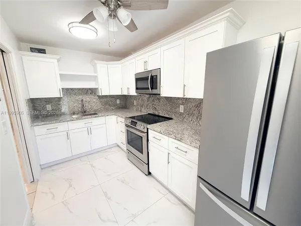 a kitchen with granite countertop a refrigerator a sink a stove and white cabinets