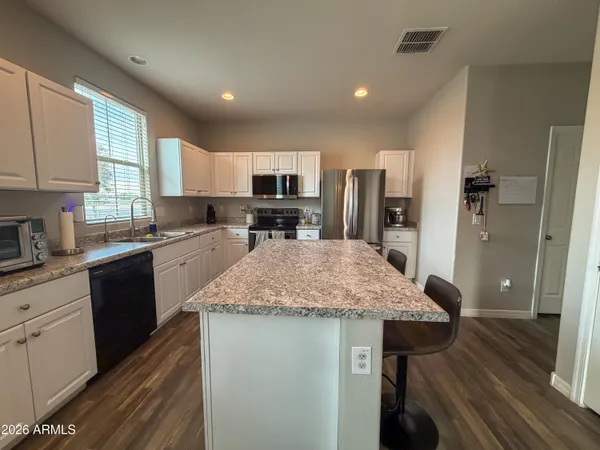 a kitchen with stainless steel appliances granite countertop a stove top oven a refrigerator a sink and white cabinets with wooden floor