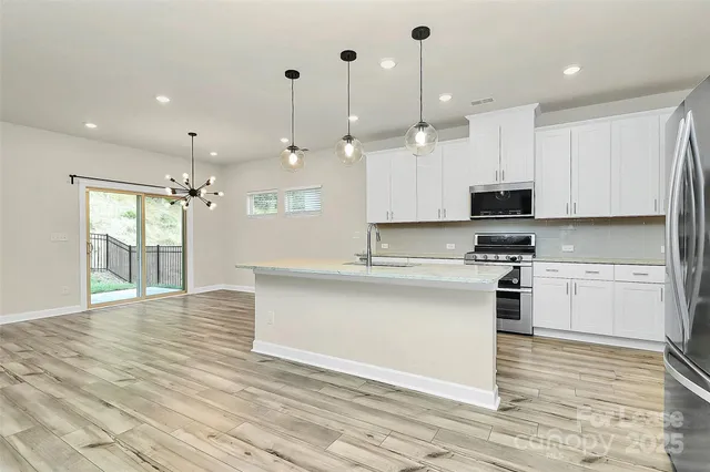 a large kitchen with granite countertop a stove a sink and white cabinets with wooden floor