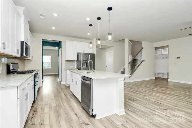 a large kitchen with stainless steel appliances a stove top oven a sink dishwasher and white cabinets with wooden floor