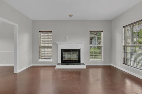 an empty room with wooden floor fireplace and windows