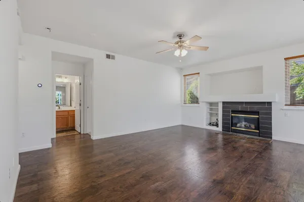 an empty room with wooden floor a ceiling fan a fireplace and windows