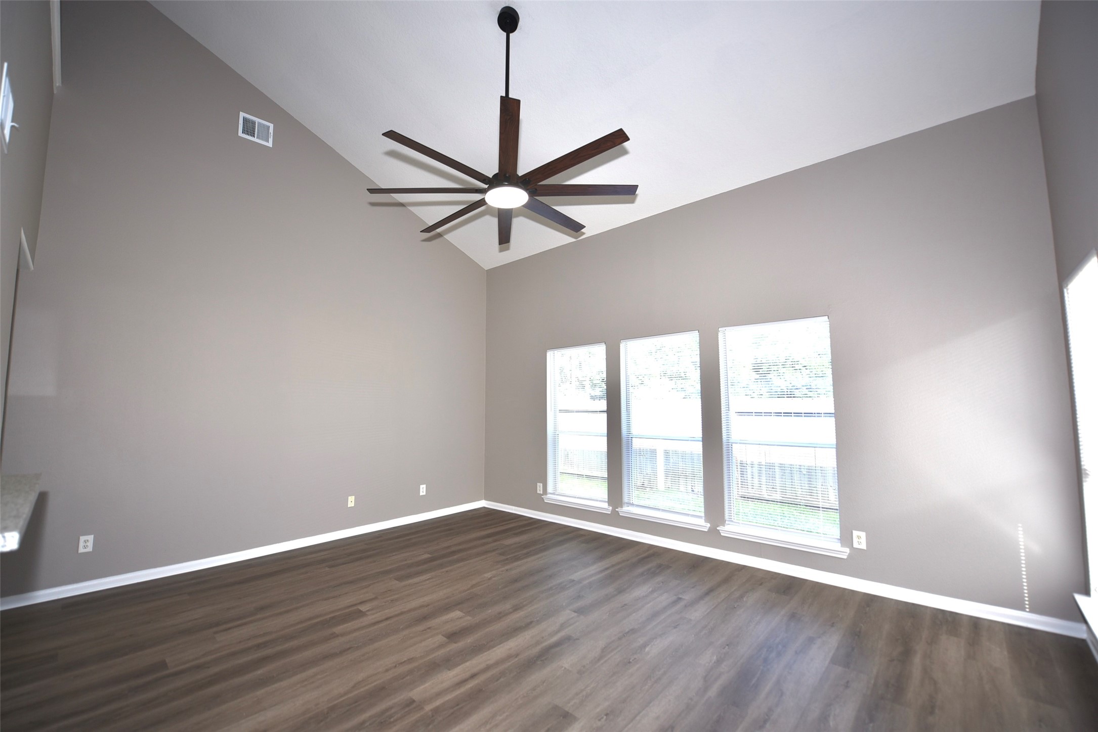 9611 Babbling Spring Court Tomball, TX 77375 - Photo 9 of 31 This spacious room features high vaulted ceilings with a modern ceiling fan, large windows for ample natural light, and sleek wood flooring, creating an inviting and contemporary living space.
