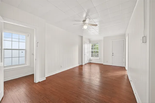 an empty room with wooden floor chandelier fan and windows