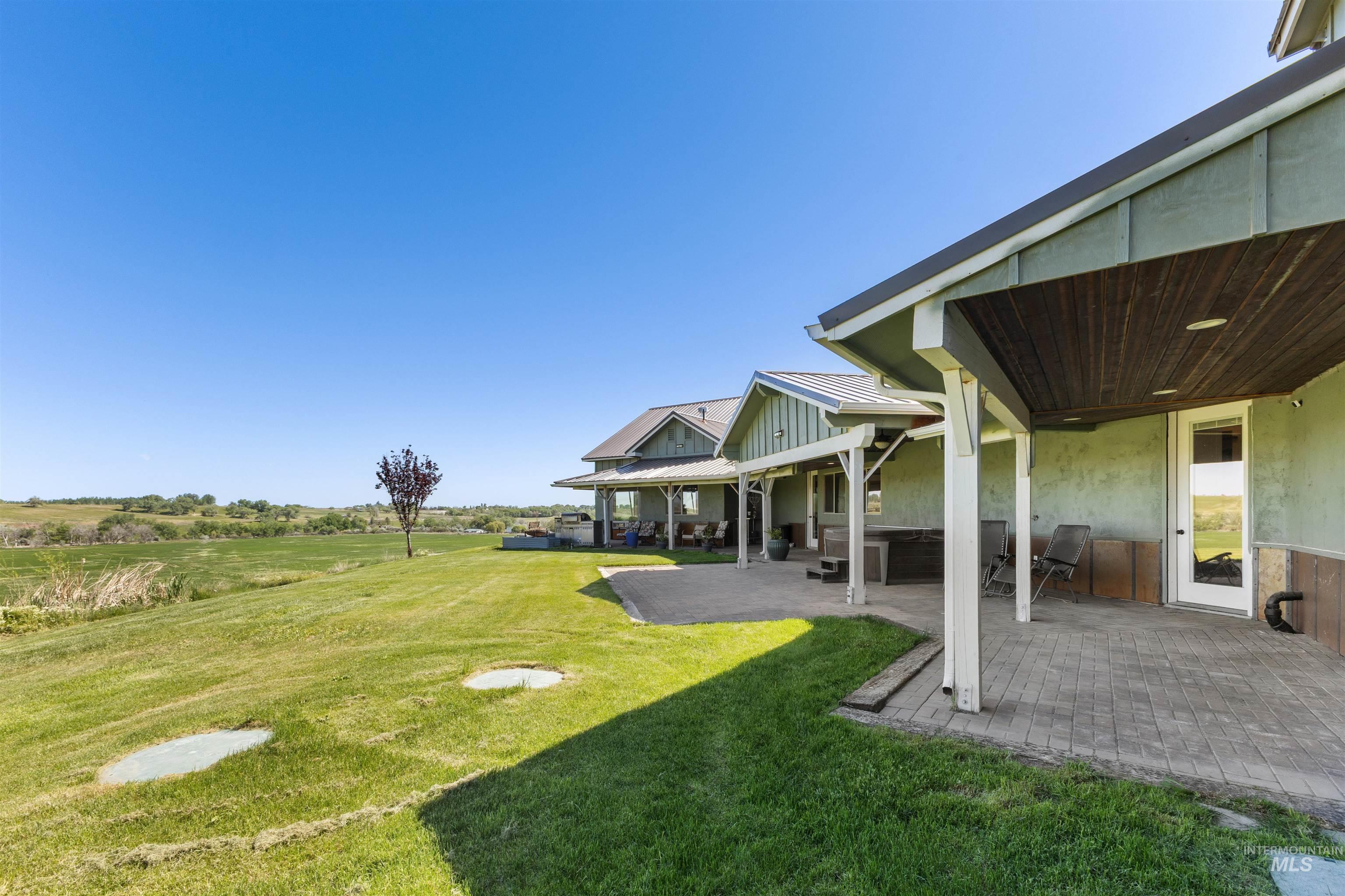 1030 Desert Glen Road Adrian, OR 97901 - Photo 8 of 47 Expansive green lawn with a mature tree, bordered by a large paved patio featuring a wood-panel ceiling under an extended roofline