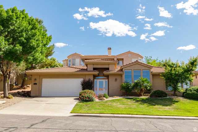 Stucco exterior residence with a tiled roof, a prominent arched entry, a two-car garage, and established landscaping featuring mature trees and shrubbery