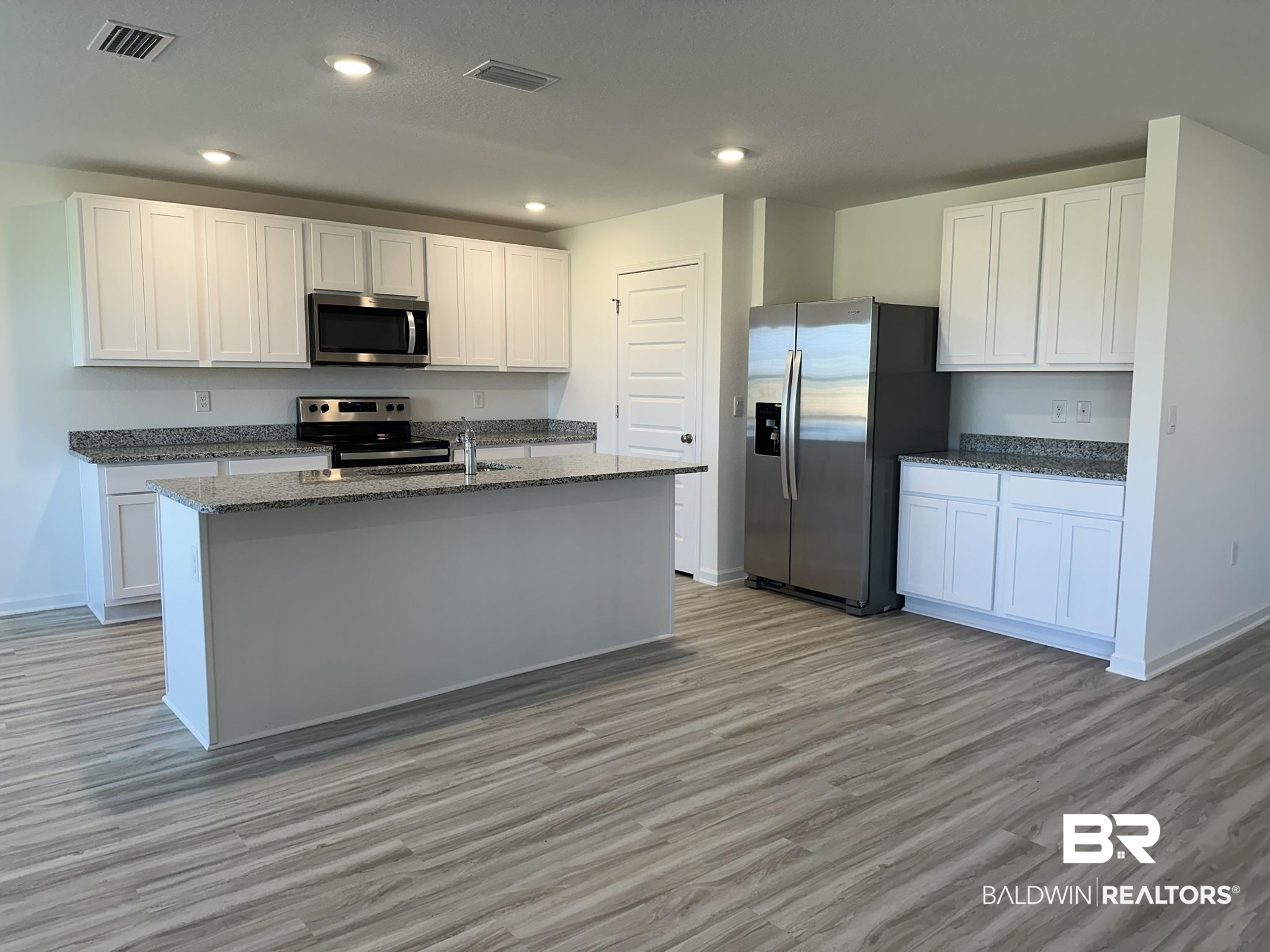 22227 Aleutian Avenue Foley, AL 36535 - Photo 7 of 64 Kitchen with white cabinets, light hardwood / wood-style flooring, a kitchen island with sink, appliances with stainless steel finishes, and dark stone countertops
