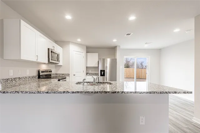 a large kitchen with granite countertop a stove a sink a refrigerator and white cabinets with wooden floor