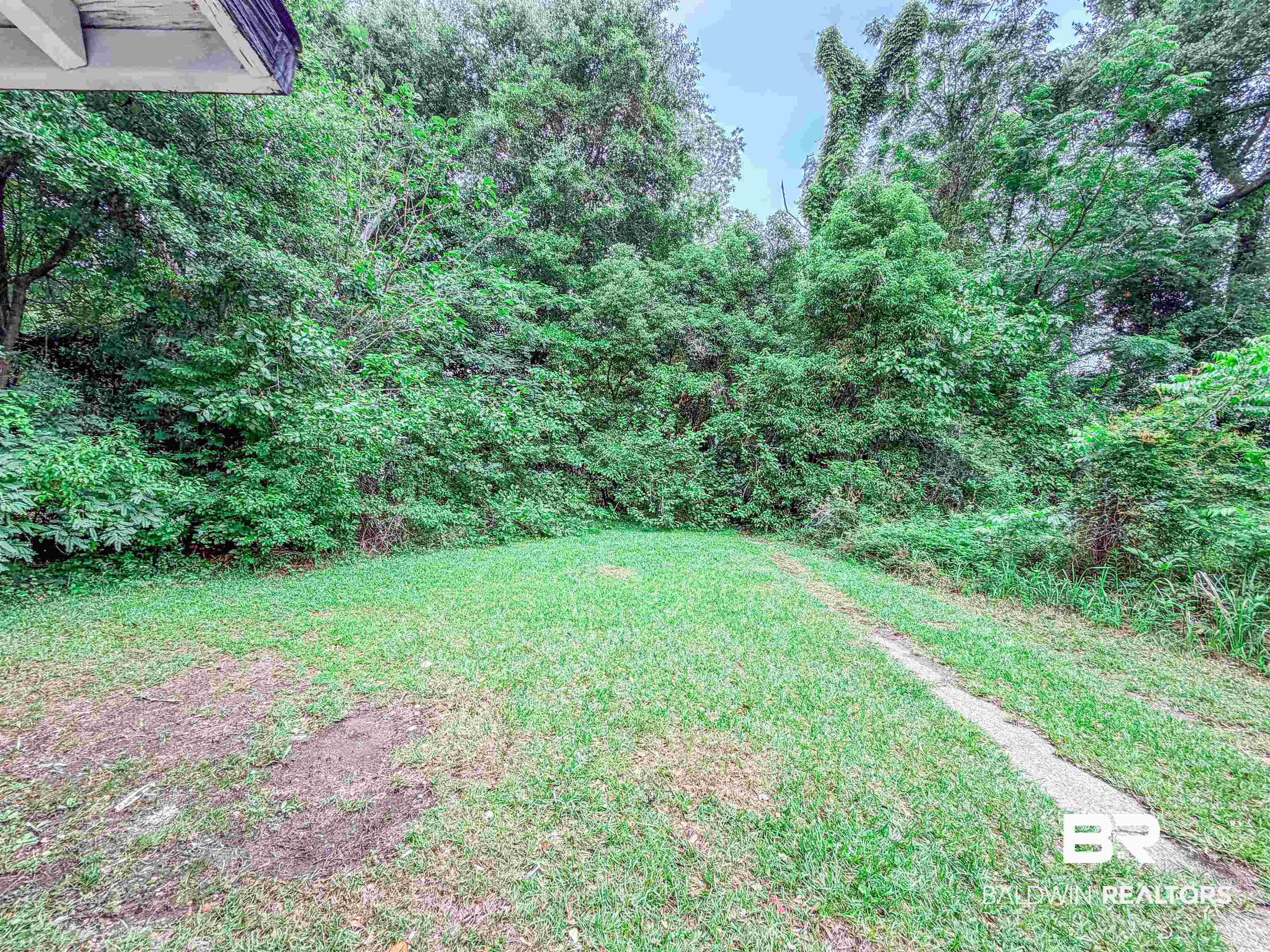 38 Flock Avenue Mobile, AL 36610 - Photo 24 of 27 Expansive green space featuring a grass lawn, mature trees, dense foliage, a concrete strip, and a partial view of an exterior architectural element