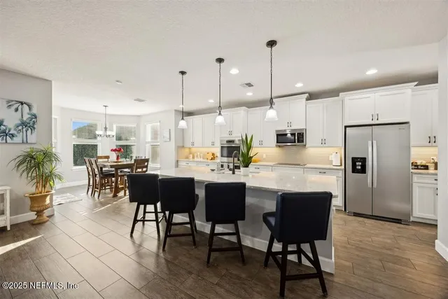 a kitchen with stainless steel appliances kitchen island granite countertop a dining table chairs and a refrigerator